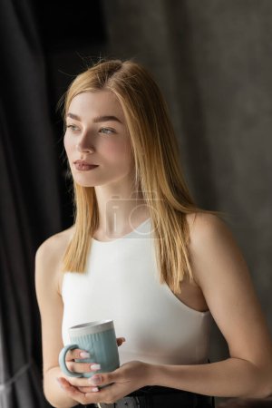 Portrait of young blonde woman holding cup of coffee at home 