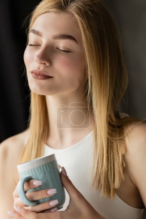 Pleased blonde woman holding cup of coffee at home in morning 