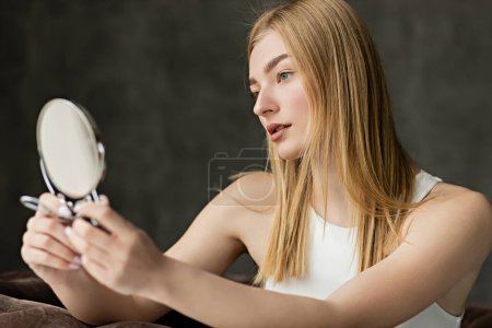 Blonde woman in top holding blurred mirror at home 