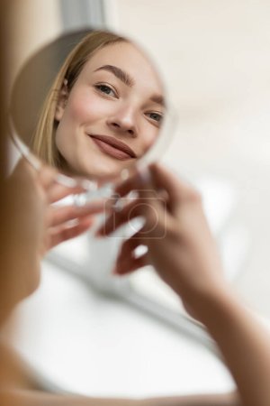 Smiling woman reflecting in blurred mirror at home 