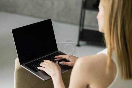 Freelancer rubia borrosa usando portátil con pantalla en blanco en casa 