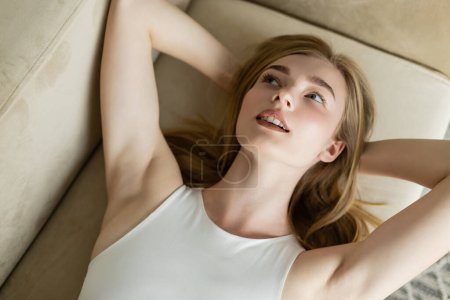 Junge blonde Frau entspannt sich zu Hause auf beiger Couch 