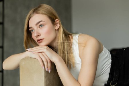 Pensive blonde woman looking away while sitting on sofa at home 