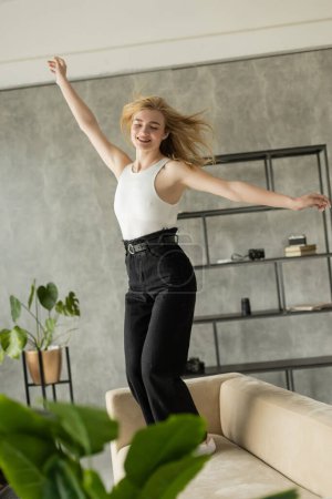 Photo for Excited woman with closed eyes and outstretched hands dancing on sofa at home - Royalty Free Image