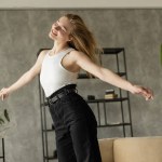 cheerful blonde woman dancing with closed eyes while having fun at home