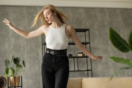 blonde woman with outstretched hands pouting lips while dancing at home