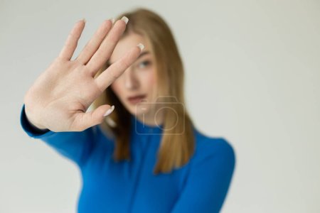 blurred blonde woman showing stop sign with outstretched hand isolated on grey