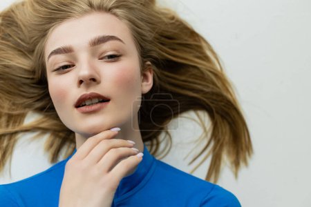 Photo for Top view of blonde woman touching chin and looking away while lying on grey background - Royalty Free Image