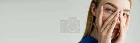 Téléchargez les photos : Portrait de femme blonde couvrant le visage avec les mains et regardant la caméra isolée sur gris, bannière - en image libre de droit