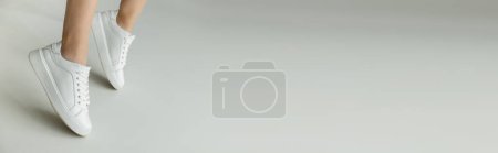 Photo for Cropped view of woman in white laced sneakers standing on tiptoes on grey background with copy space, banner - Royalty Free Image
