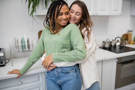 Téléchargez les photos : Heureuse lesbienne femme embrassant joyeuse afro-américaine copine dans la cuisine - en image libre de droit