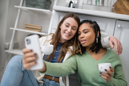 Photo for Lesbian african american woman taking selfie with girlfriend in kitchen - Royalty Free Image