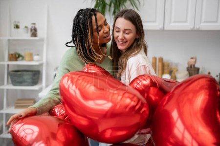 Téléchargez les photos : Heureux interracial et lesbiennes les femmes près de ballons rouges sur la Saint-Valentin - en image libre de droit