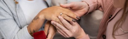 Téléchargez les photos : Vue recadrée de femme lesbienne portant la bague de fiançailles sur le doigt de la petite amie afro-américaine, bannière - en image libre de droit