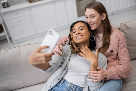 tätowierte afrikanisch-amerikanische lesbische Frau zeigt Verlobungsring, während sie Selfie mit Partner macht 