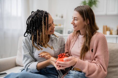 Téléchargez les photos : Heureux afro-américain et lesbienne femme donnant en forme de coeur cadeau à petite amie - en image libre de droit