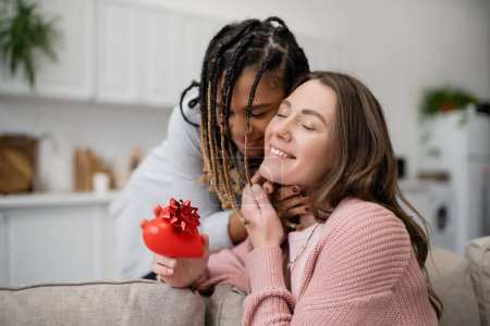 Téléchargez les photos : Africaine américaine lesbienne femme étreignant joyeuse petite amie avec rouge en forme de coeur présent - en image libre de droit