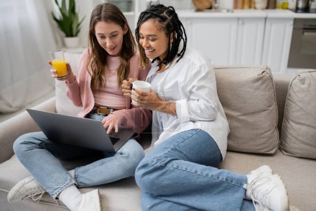 glücklich afrikanisch-amerikanische lesbische Frau hält Tasse Kaffee in der Nähe Freundin mit Laptop während der Arbeit von zu Hause aus 