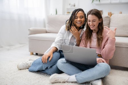 tattooed african american woman smiling while showing engagement ring near girlfriend during video call 