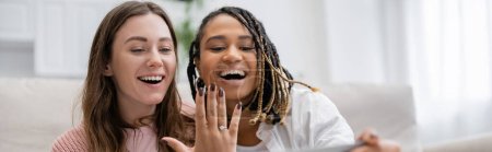 Téléchargez les photos : Lesbienne afro-américaine femme montrant bague de fiançailles près de petite amie étonnée, bannière - en image libre de droit