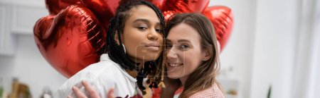 multiethnic lesbian women looking at camera near balloons on valentines day, banner 