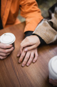 Cropped view of woman in blanket touching hand of boyfriend near coffee to go in outdoor cafe  Longsleeve T-shirt #627166436