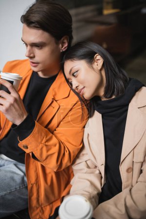 Téléchargez les photos : Élégante femme asiatique tenant café flou pour aller près petit ami sur la terrasse du café - en image libre de droit
