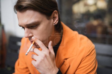 Junger brünetter Mann raucht Zigarette im Freien 