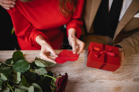 Draufsicht von beschnittenem Mann mit Geschenk in der Nähe seiner Freundin mit roter herzförmiger Grußkarte am Valentinstag 