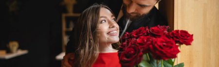 Foto de Hombre barbudo sosteniendo ramo de rosas rojas cerca de novia feliz en día de San Valentín, bandera - Imagen libre de derechos