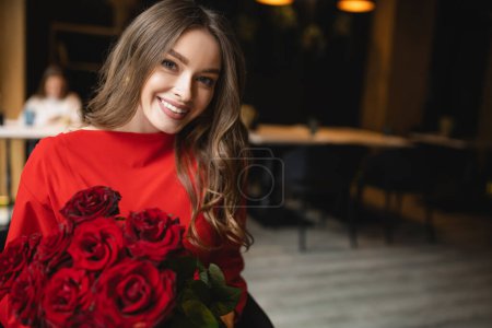 Foto de Bonita mujer joven sosteniendo ramo de rosas rojas y sonriendo el día de San Valentín - Imagen libre de derechos