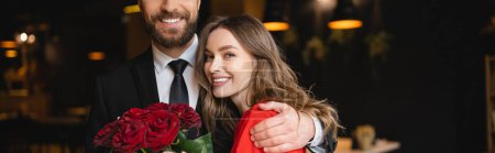 bärtiger Mann umarmt glückliche Freundin am Valentinstag mit einem Strauß roter Rosen, Banner 