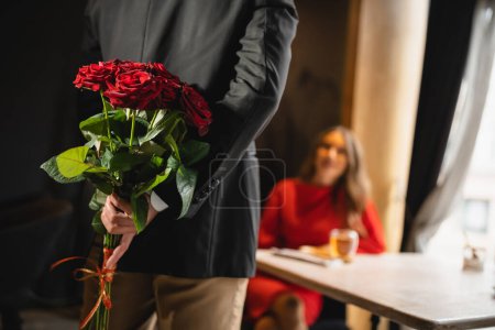 Ausgeschnittene Ansicht eines Mannes, der am Valentinstag einen Strauß roter Rosen hinter dem Rücken versteckt 