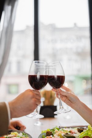 Photo pour Vue partielle du couple cliquetis verres avec du vin rouge pendant la célébration le jour de la Saint-Valentin - image libre de droit