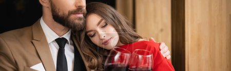 young woman and bearded man clinking glasses with red wine during celebration on valentines day, banner 