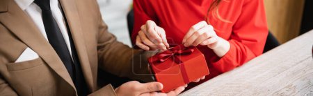 cropped view of man in formal wear holding present while woman in red dress pulling ribbon on valentines day, banner  Stickers 631516326