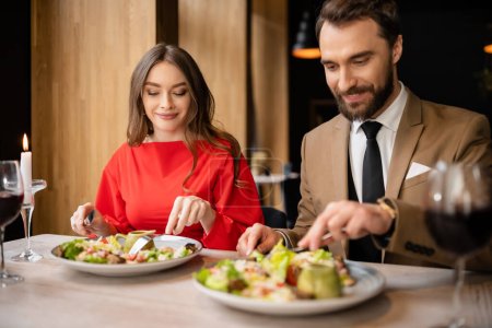 glückliches junges Paar in festlicher Kleidung schaut sich bei der Feier am Valentinstag leckeren Salat an 