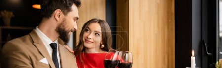smiling young woman and man clinking glasses with red wine during celebration on valentines day, banner 