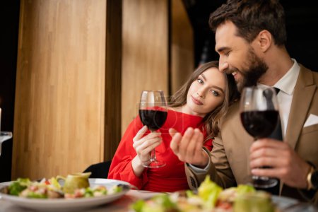 young woman and cheerful man holding glasses with red wine during celebration on valentines day 