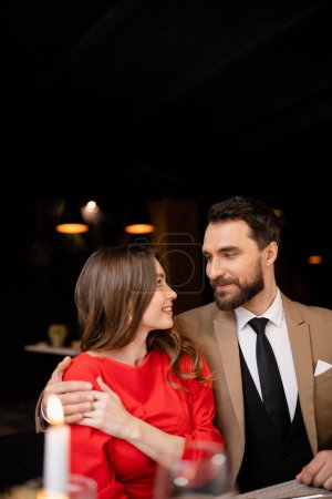 bearded man hugging cheerful young woman in red dress on valentines day 