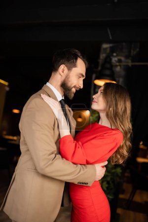 alegre hombre y mujer en traje festivo abrazándose mientras se miran el día de San Valentín 