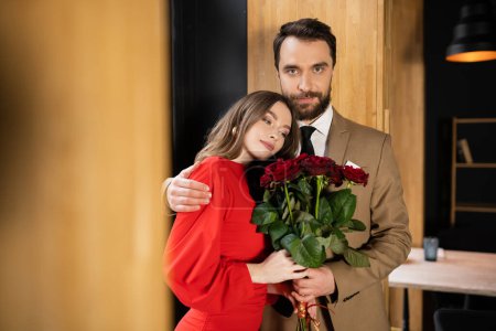 young woman in dress holding red roses and leaning on boyfriend on valentines day  