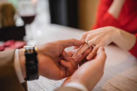 cropped view of man making proposal and wearing engagement ring on finger of girlfriend on valentines day 