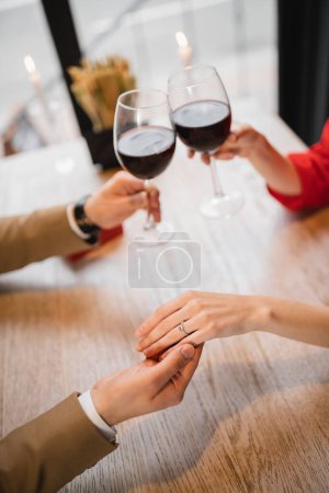 Foto de Vista recortada de la mujer con anillo de compromiso en el dedo tintineo vasos de vino con novio en el día de San Valentín - Imagen libre de derechos