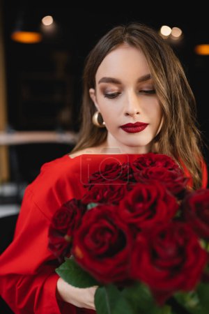 Foto de Bonita mujer joven mirando rosas rojas en el día de San Valentín - Imagen libre de derechos