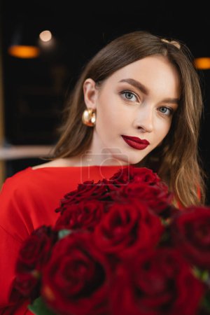 Foto de Bonita joven sosteniendo rosas rojas y mirando a la cámara en el día de San Valentín - Imagen libre de derechos