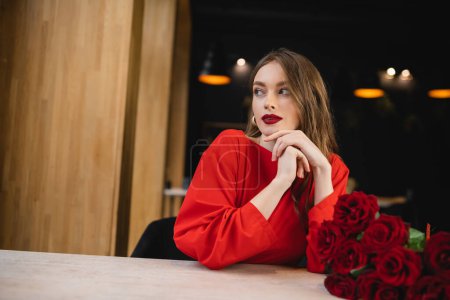 Foto de Mujer joven soñadora mirando hacia otro lado cerca de rosas rojas en el día de San Valentín - Imagen libre de derechos