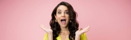 Photo for Amazed brunette woman with open mouth looking at camera and showing wow gesture isolated on pink, banner - Royalty Free Image