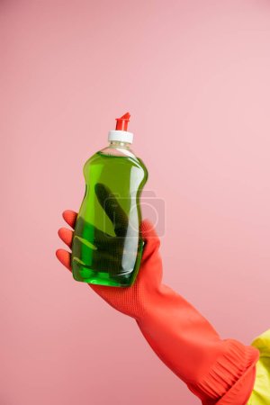 Foto de Vista parcial de la mujer en guante de goma rojo sosteniendo la botella con detergente verde aislado en rosa - Imagen libre de derechos