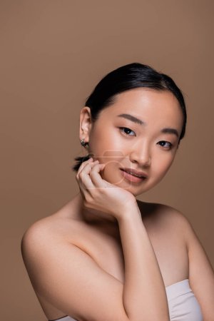 Portrait of smiling asian model looking at camera isolated on brown 